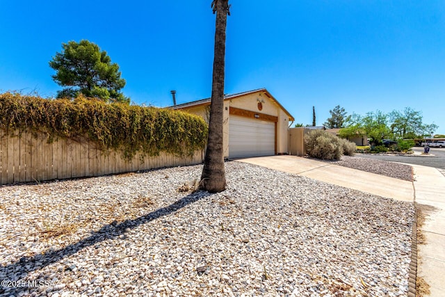 view of front facade with stucco siding, a garage, fence, and concrete driveway