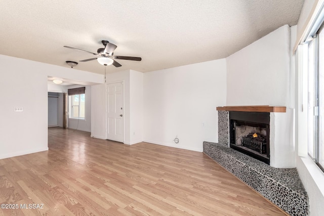 unfurnished living room with light wood-style floors, a ceiling fan, a textured ceiling, and a fireplace with raised hearth