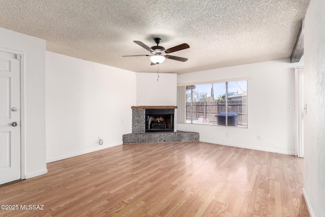 unfurnished living room with a fireplace with raised hearth, a textured ceiling, a ceiling fan, baseboards, and wood finished floors