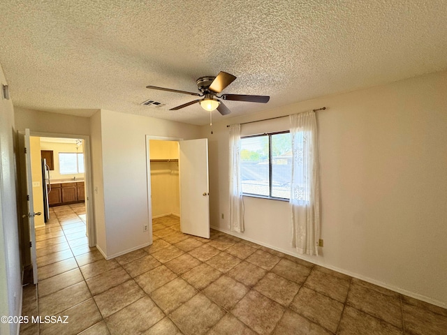 unfurnished bedroom with a walk in closet, a closet, a textured ceiling, and visible vents