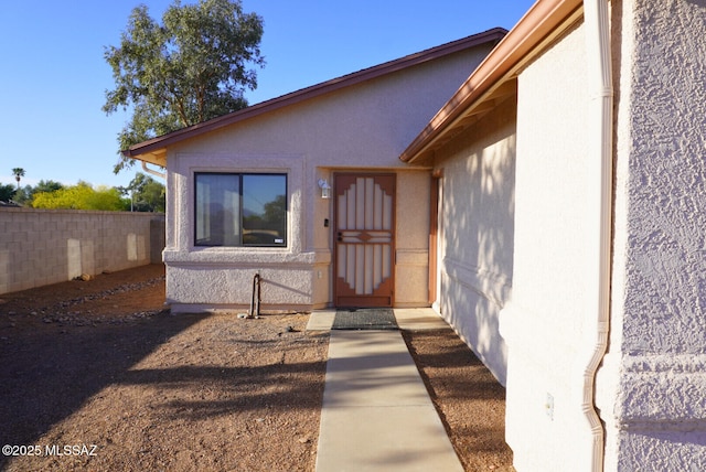 view of exterior entry with stucco siding and fence