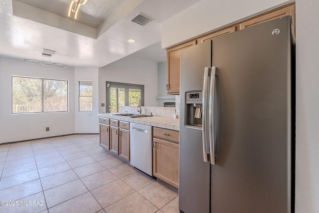 kitchen with a sink, stainless steel appliances, tile countertops, visible vents, and light tile patterned floors