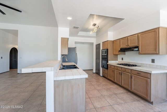 kitchen with a sink, black appliances, visible vents, under cabinet range hood, and tile counters