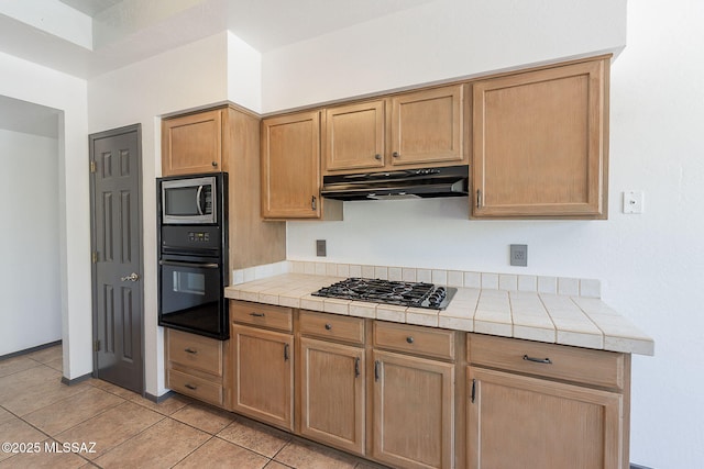 kitchen featuring under cabinet range hood, tile counters, black appliances, and light tile patterned floors