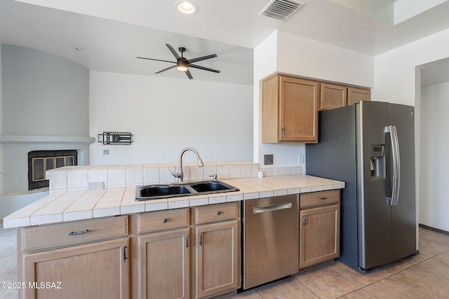 kitchen with ceiling fan, visible vents, a sink, tile counters, and appliances with stainless steel finishes