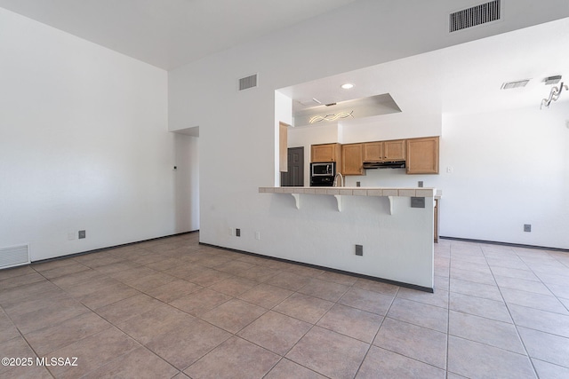 kitchen with tile counters, visible vents, under cabinet range hood, and a kitchen bar