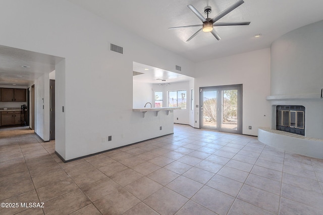 unfurnished living room with a ceiling fan, a glass covered fireplace, light tile patterned floors, and visible vents
