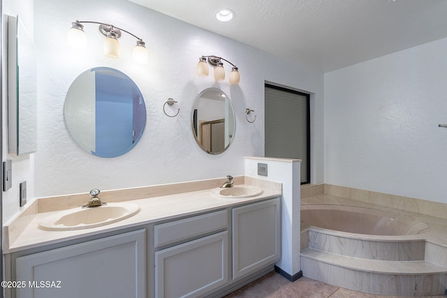 full bathroom with double vanity, a garden tub, a textured wall, and a sink