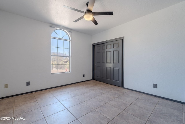 unfurnished bedroom with baseboards, a closet, light tile patterned floors, and ceiling fan