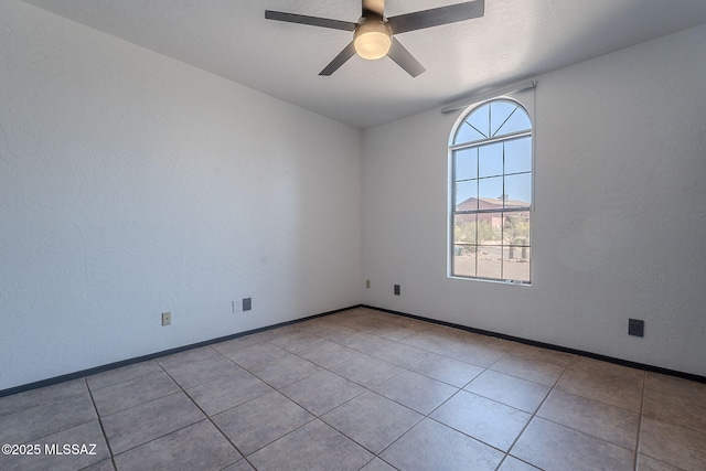 tiled empty room featuring baseboards and a ceiling fan