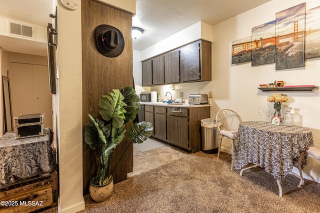 kitchen featuring light countertops, baseboards, dark brown cabinetry, and visible vents