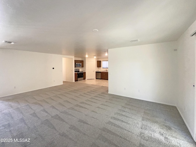 unfurnished living room featuring baseboards, visible vents, and light carpet