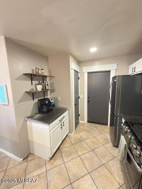 kitchen with white cabinets, light tile patterned flooring, dark countertops, and stainless steel gas stove
