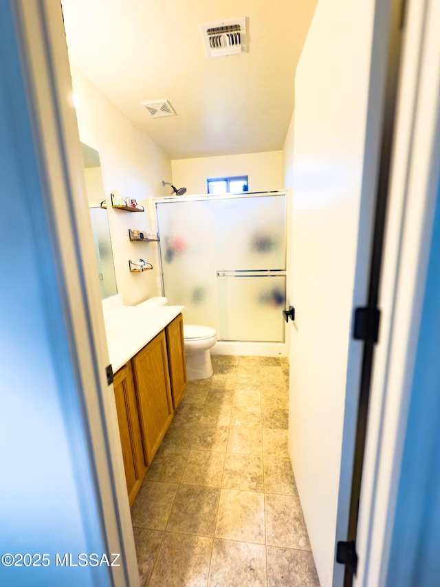 bathroom with visible vents, a shower with door, toilet, and vanity