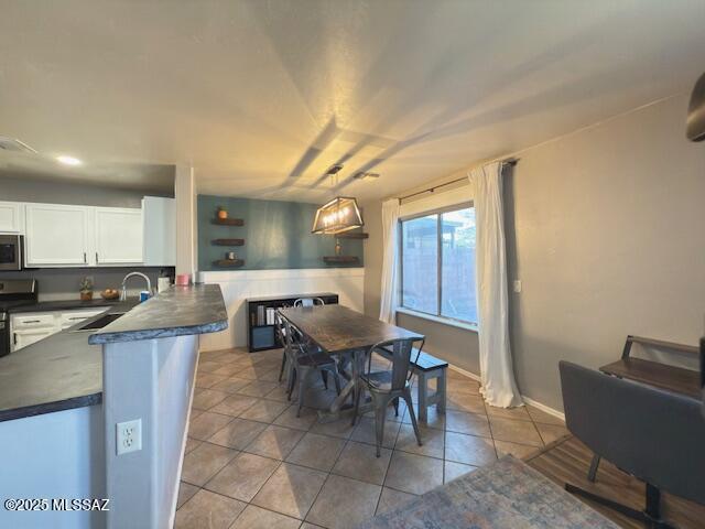 kitchen with dark countertops, white cabinetry, stainless steel microwave, a sink, and light tile patterned floors
