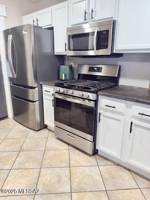 kitchen with white cabinetry, light tile patterned floors, dark countertops, and stainless steel appliances