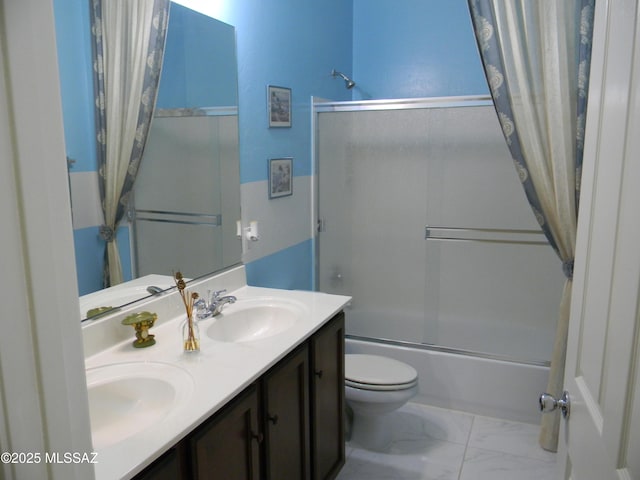 bathroom featuring double vanity, marble finish floor, toilet, bath / shower combo with glass door, and a sink