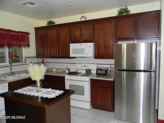 kitchen featuring decorative backsplash, a kitchen island, visible vents, a sink, and white appliances