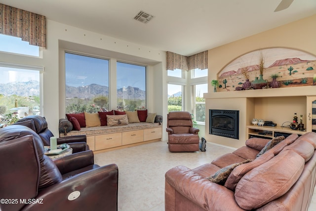 living room featuring visible vents, a mountain view, a glass covered fireplace, and ceiling fan