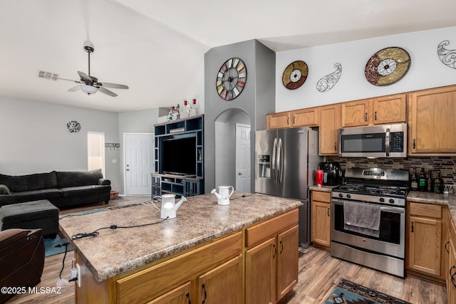 kitchen featuring decorative backsplash, open floor plan, a ceiling fan, light wood finished floors, and stainless steel appliances