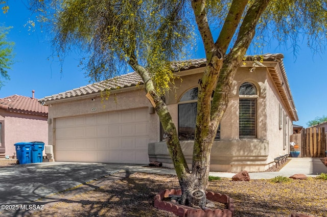 mediterranean / spanish-style house with fence, a tile roof, a garage, stucco siding, and concrete driveway