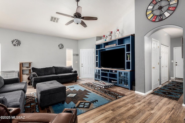 living area with arched walkways, a ceiling fan, baseboards, wood finished floors, and visible vents