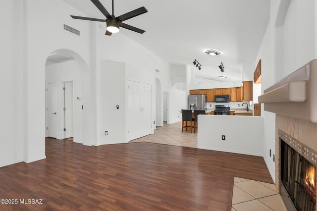 114 W Freddie Canyon Way, Oro Valley, AZ 85755 - unfurnished living room with ceiling fan, arched walkways, high vaulted ceiling, a tile fireplace, and visible vents