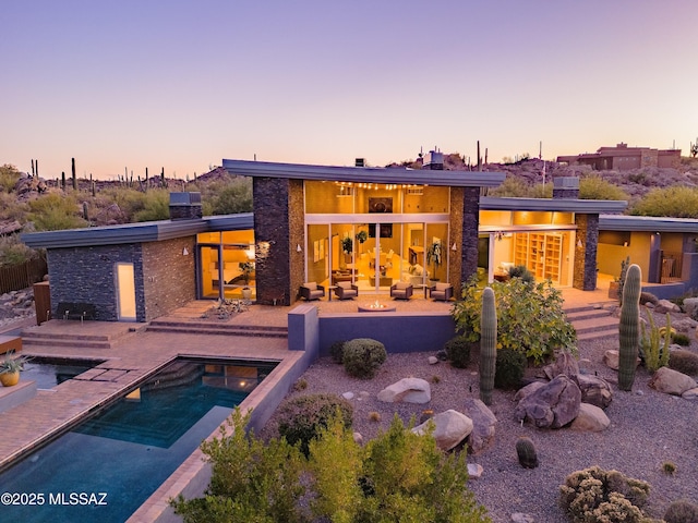 back of house at dusk with a jacuzzi, a chimney, a patio area, and an outdoor pool