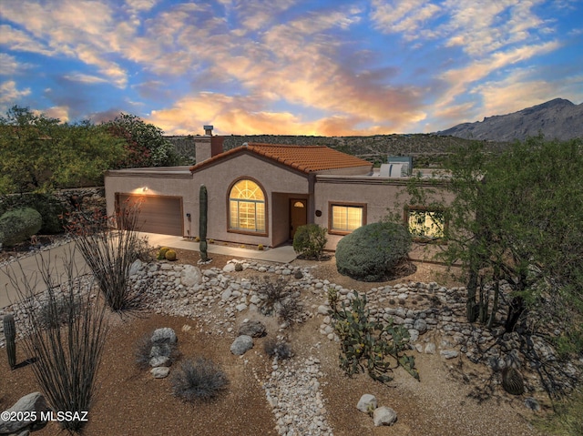 mediterranean / spanish house featuring a garage, stucco siding, a mountain view, a chimney, and a tiled roof