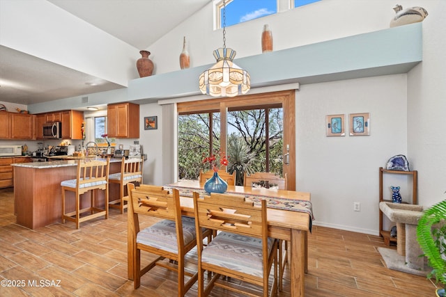 dining space featuring light wood-style floors, baseboards, a wealth of natural light, and high vaulted ceiling