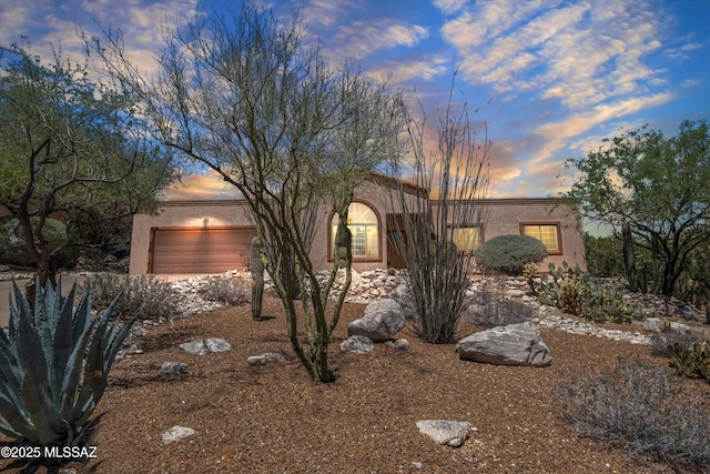pueblo revival-style home featuring an attached garage and stucco siding