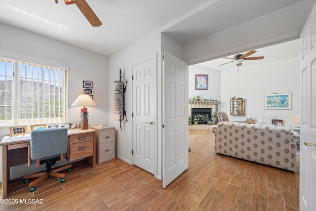 home office with ceiling fan, a fireplace, and light wood-style flooring