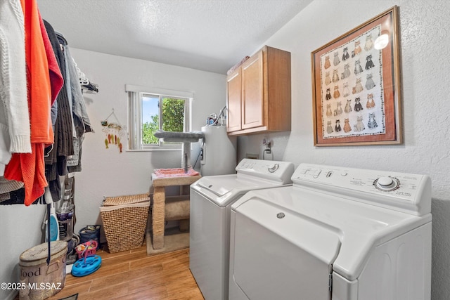 laundry room with washing machine and dryer, a textured ceiling, cabinet space, light wood finished floors, and water heater