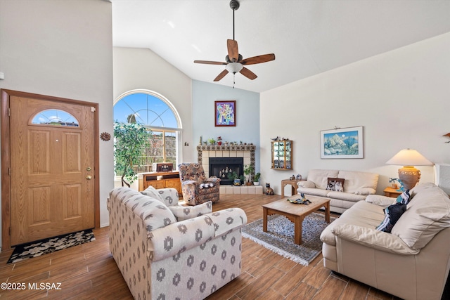 living room with high vaulted ceiling, a ceiling fan, wood finished floors, and a tile fireplace