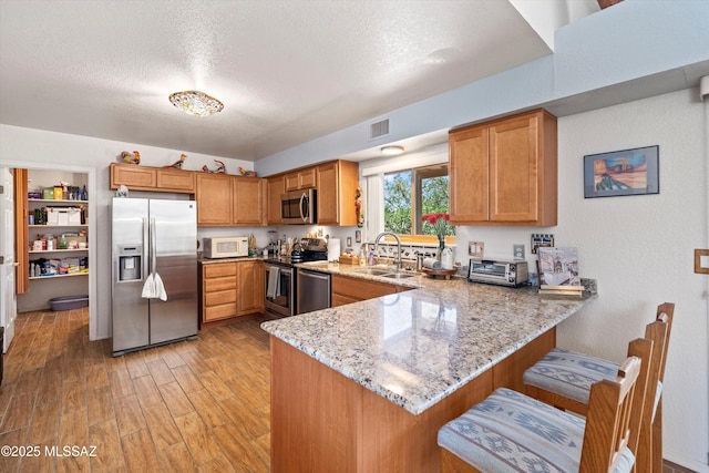 kitchen with visible vents, a peninsula, light stone counters, a sink, and stainless steel appliances