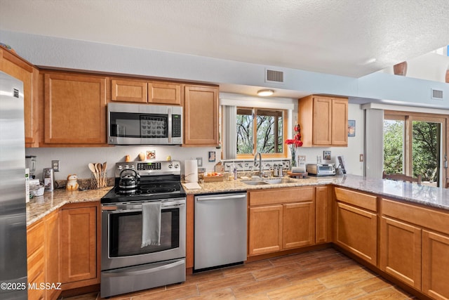 kitchen featuring visible vents, light wood-style floors, light stone counters, a sink, and stainless steel appliances