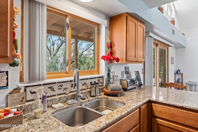 kitchen with a sink, light stone counters, brown cabinetry, and visible vents