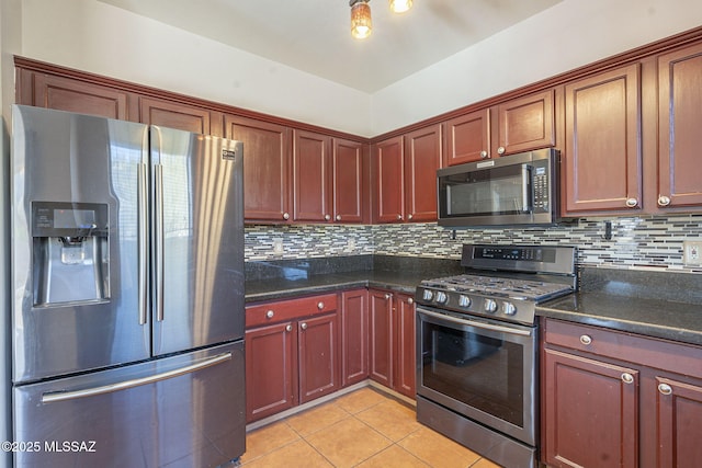 kitchen featuring dark stone counters, stainless steel appliances, light tile patterned floors, reddish brown cabinets, and backsplash