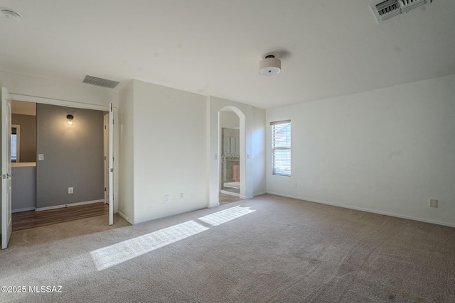 unfurnished bedroom with carpet floors, baseboards, arched walkways, and visible vents