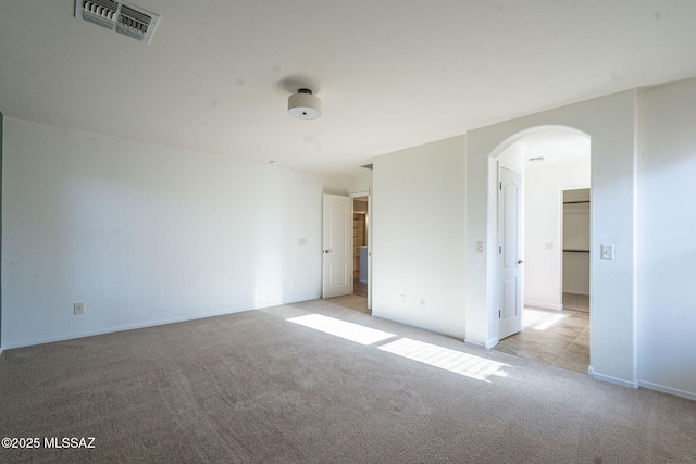 unfurnished bedroom with visible vents, arched walkways, baseboards, and light carpet