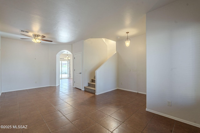 unfurnished room featuring ceiling fan, arched walkways, baseboards, tile patterned floors, and stairs