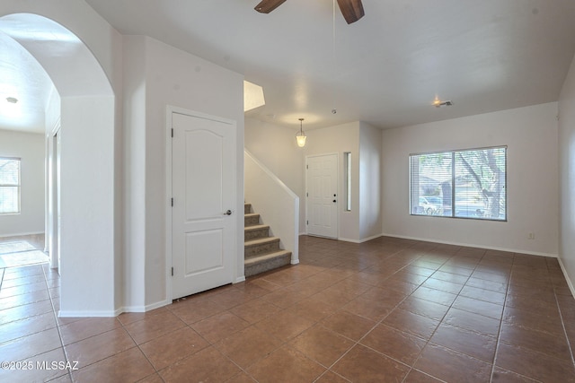 unfurnished room with visible vents, stairs, arched walkways, tile patterned floors, and a ceiling fan