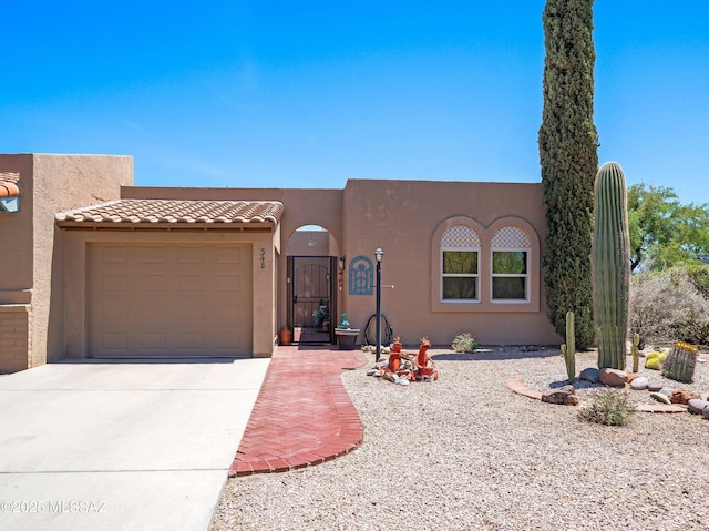 pueblo-style house with concrete driveway, stucco siding, and a garage