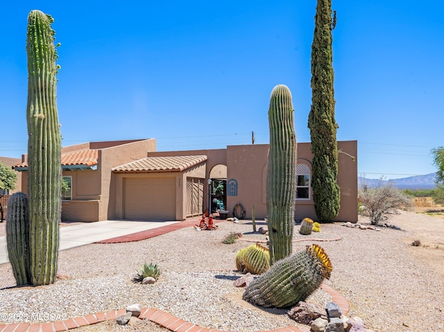 pueblo-style home with a garage, stucco siding, concrete driveway, a mountain view, and a tile roof