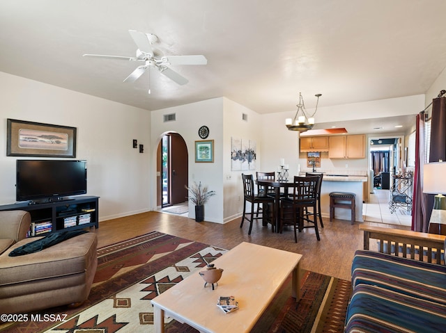 living room featuring light wood finished floors, arched walkways, ceiling fan with notable chandelier, baseboards, and visible vents