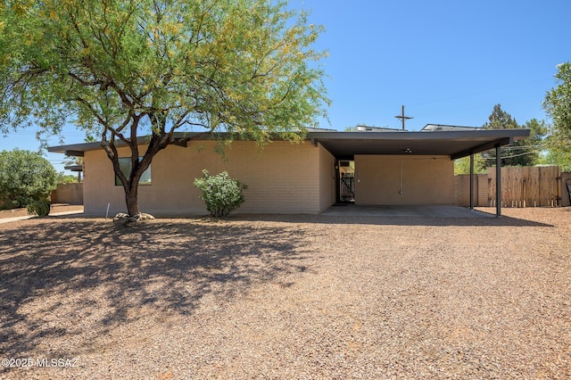 view of front facade featuring fence, a carport, and gravel driveway