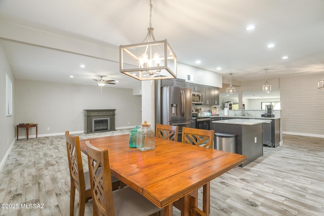 dining area with baseboards, light wood-style floors, recessed lighting, a fireplace with flush hearth, and ceiling fan with notable chandelier