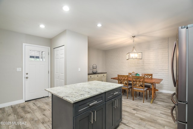 kitchen with baseboards, freestanding refrigerator, light wood-style flooring, and brick wall