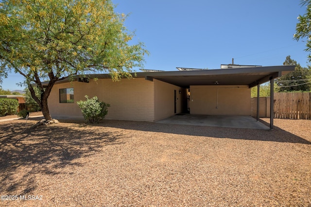 view of front of house with dirt driveway, fence, and an attached carport