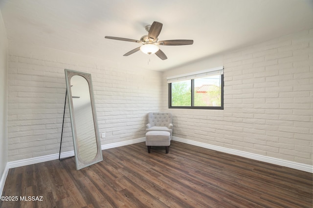 unfurnished room with baseboards, ceiling fan, wood finished floors, and brick wall